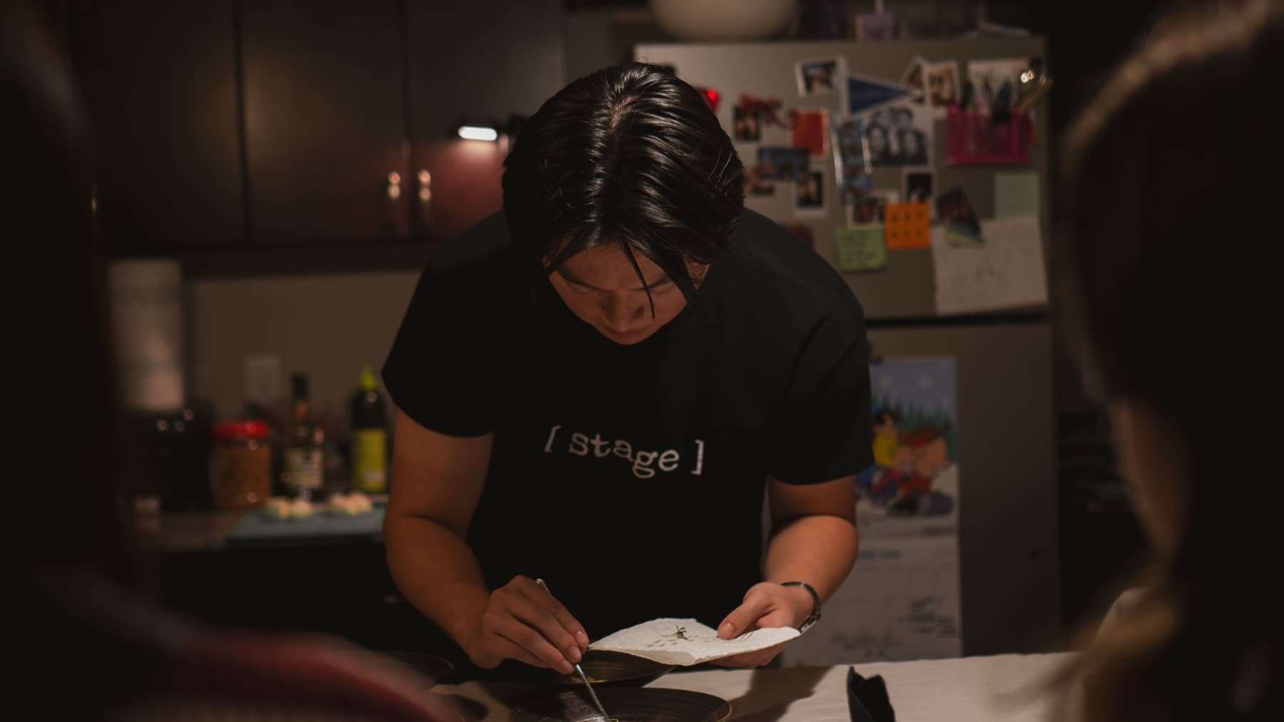 A chef in a [ stage ] shirt finishing a plate