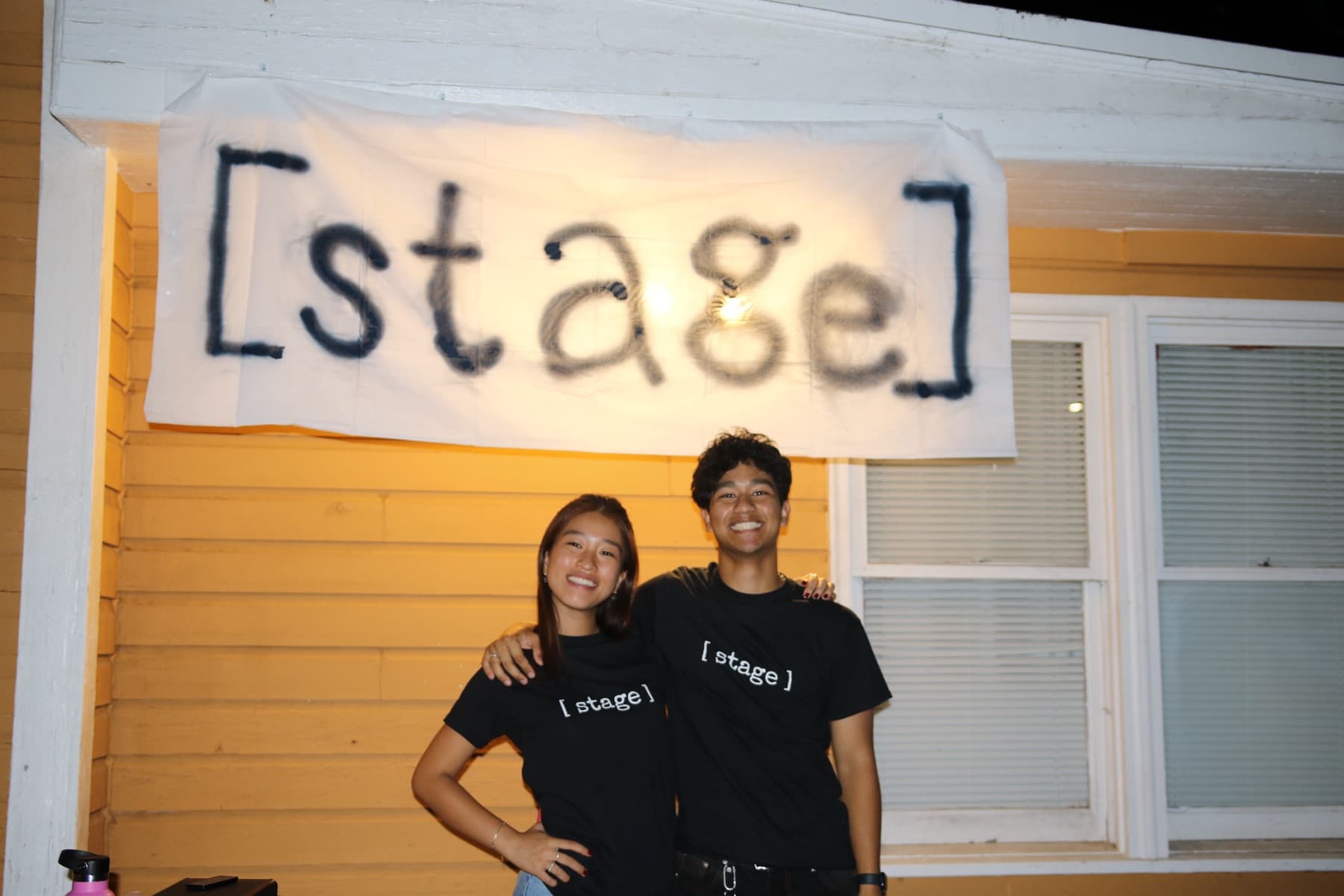 Two chefs under a hand-painted [ stage ] banner
