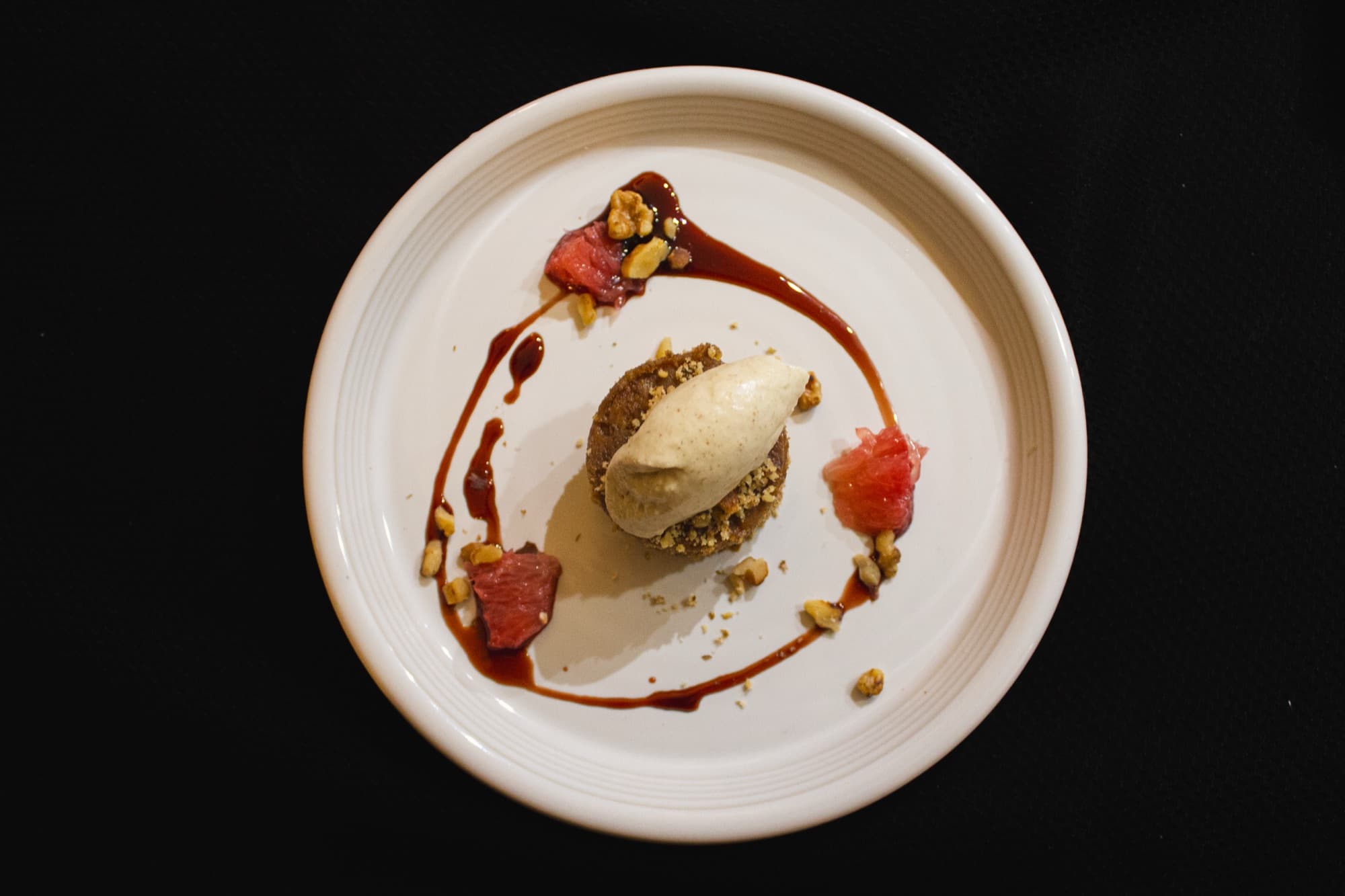 A plated dessert quenelle with fruit and sauce